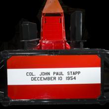 Straight metal seat attached to the middle of a rocket sled. Col. John Paul Stapp December 10 1954 is painted on the seat. 