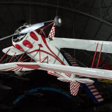 White and red painted single-engine aerobatic and military trainer biplane hanging in the museum.