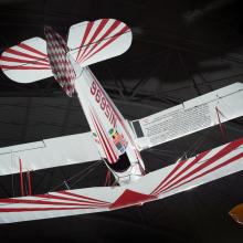 White and red painted single-engine aerobatic and military trainer biplane hanging in the museum.