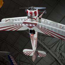 White and red painted single-engine aerobatic and military trainer biplane hanging in the museum.