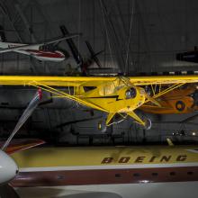 Yellow monoplane hanging in the museum with other planes in view