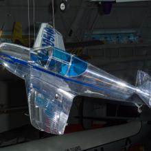 Metal plane with wood propeller and blue-tinted windows hanging in the museum. 