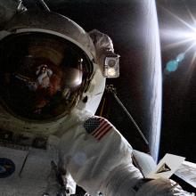 A photograph of an astronaut in his space suit, with a large spherical shape in the background.