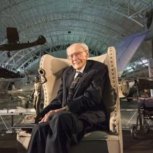 Bob Hoover sitting in a chair amongst the exhibitions at the Udvar-Hazy Center. 