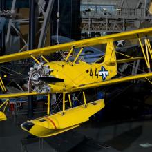 Bright yellow bi-plane with hand crank start hanging in the Steven F. Udvar-Hazy Center.