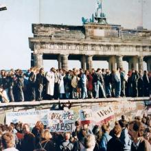 A crowd stands on the Berlin wall. 