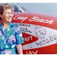 Woman posing next to the nose of a small airplane.