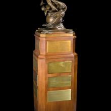 A bronze sculpture of a globe, two male and one female figures rising from the globe, sitting atop a tall walnut base.