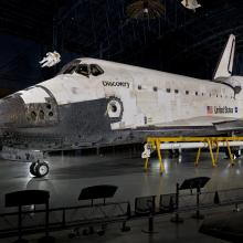 Space Shuttle Discovery displayed in a hangar with the United States flag in the background.