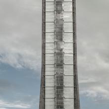 Partial view of the air traffic control at Oslo Airport in Norway. This portion of the tower has dark gray-colored steel sides which open up to possess lighter gray brick-like patterns in between another section of darker gray steel.