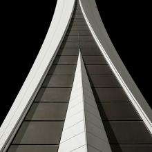 Partial view of the base of an air traffic control tower in Dubai. The base features a gray concrete stacking pattern with white ornate edges and details.