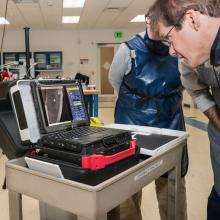 A Musuem conservator looks at a small laptop computer, where they view X-ray images of a spaceship studio model.