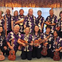 A large ensemble of ukulele players pose together with their ukuleles.