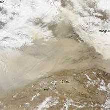 Satellite view of a desert near the border of China and Mongolia. The view is partially obscured by clouds on the top and bottom of the view as well as a dust storm in the center.