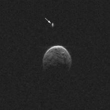 Radar image of an asteroid during its nearest approach to Earth. The asteroid's singular moon is pointed out using a white arrow.