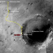 A partial, black and white satellite view of Mars with a yellow line describing the movement made by Opportunity, a Mars rover, between multiple craters.