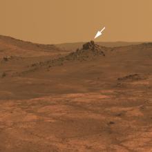 A hilly landscape on Mars with a small white arrow pointing to a crater named after a historic aircraft, the "Spirit of St. Louis".