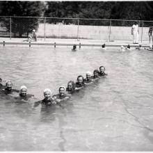 A group of female pilots in training during World War II swim together in a triangle formation in a pool.