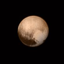 Disk view of Pluto, showing a brown planet with a heart-like shape coloration on the lower right quadrant of the dwarf planet.