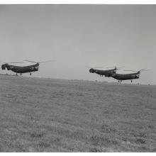 Three helicopters with two sets of propellors apiece vertically fly together during an airshow.