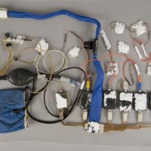 A during-conservation view of an blue Apollo program medical instrumentation harness. Majority of the harness and various parts have been removed from its previous white board.