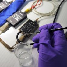 A Museum conservation specialist (seen wearing a purple glove) applies a coat of acrylic resin in the process of cleaning an Apollo program medical instrumentation harness.