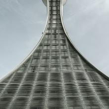 Air traffic control tower with a vial-shaped support structure that expands at the bottom from a narrow top. The support structure looks to be made from sections of steel.