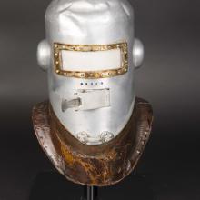 Frontal view of the first pressure helmet. The helmet is made from metal and is experiencing white-colored corrosion, requiring conservation treatment.