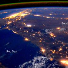 A partial satellite-style view of the Earth, with a focus on North Africa and the Middle East at night. Lights can be seen throughout heavily populated areas.