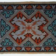 Orange, blue, and white knitted rug with intricate X-letter shape pattern.