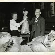 Two employees of an aeronautical corporation in the 1940s smile as one employee hands a turkey to the other employee.