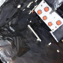 Sheets of black-colored material attached to double-sided tape are applied as part of restoring the Apollo Telescope Mount. Here, the black-covered material is placed as part of the cover of the spar.