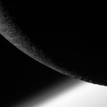 Partial view of the mostly non-illuminated Enceladus, a moon of Saturn.