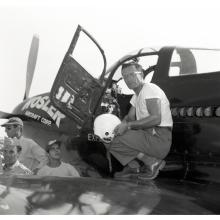 Robert Eucker, a white male aviator, stands on the wing of his aircraft. He is holding a white helmet.