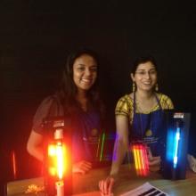 Two student volunteers host an station designed to educate children at the museum. At this station, they are holding colored gas devices.