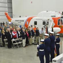 A group of people stand together for a ceremony following the restoration of an orange and white helicopter on their left .