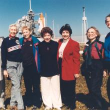 Seven women who trained to become astronauts in 1961 pose together in front of a Space Shuttle launch in 1995.