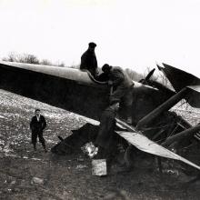 A crashed plane sits in a field and bystanders look at the plane.