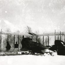 Front view of a biplane partially covered with materials as it stands on snowy ground in a snowstorm.