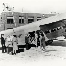 People board a light-colored commercial airplane with the United Air Lines logo on the side of the plane behind where passengers board.