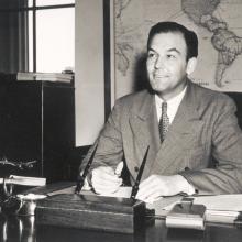 L. Welch Pogue, a white male chairman of the Civil Aeronautics Boards, poses informally as he sits at a desk.