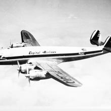 Side view of commercial aircraft in flight. Aircraft has four engines. Aircraft features "Capitol Airlines" name above the wings.