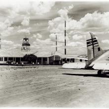 Part of the tarmac at Barreiras Airport in Brazil. Nearby are a one story building and the rear of a commercial aircraft.