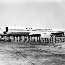 A group of Pan American Airways flight attendants board a commercial jet in a straight line.