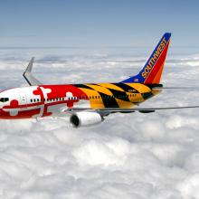 Side view of commercial aircraft in flight. Airccraft features two engines and red, white, yellow, and black Southwest Airlines livery that features the pattern of the Maryland state flag.