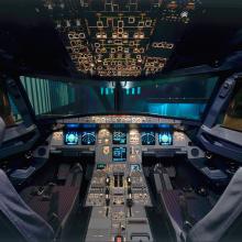 View of the front of a commercial aircraft's cockpit, with two pilot seats and the top and center panels in view.