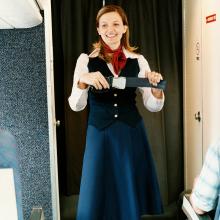 A female flight attendant holds a seat belt as part of a passenger safety demonstration.