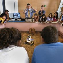 Museum visitors control a Mars rover model on a surface similar to the surface of Mars.