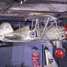 A silver biplane with red wheels and a red circle from which the propeller is mounted. The words "U.S. Marines" are on the side.