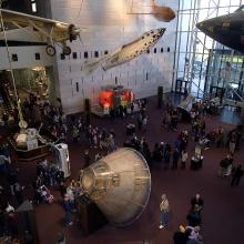 A museum exhibit with aircraft and spacecraft scattered across the floor and attached to the ceiling.